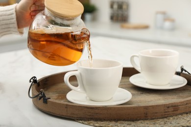 Photo of Woman pouring aromatic tea in cup at white table, closeup