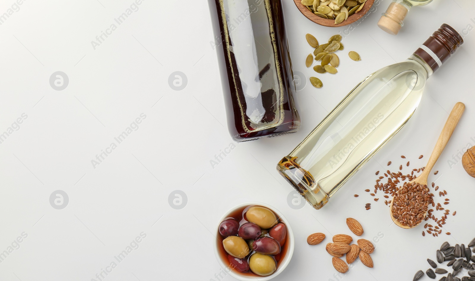 Photo of Vegetable fats. Different oils in glass bottles and ingredients on white table, flat lay. Space for text