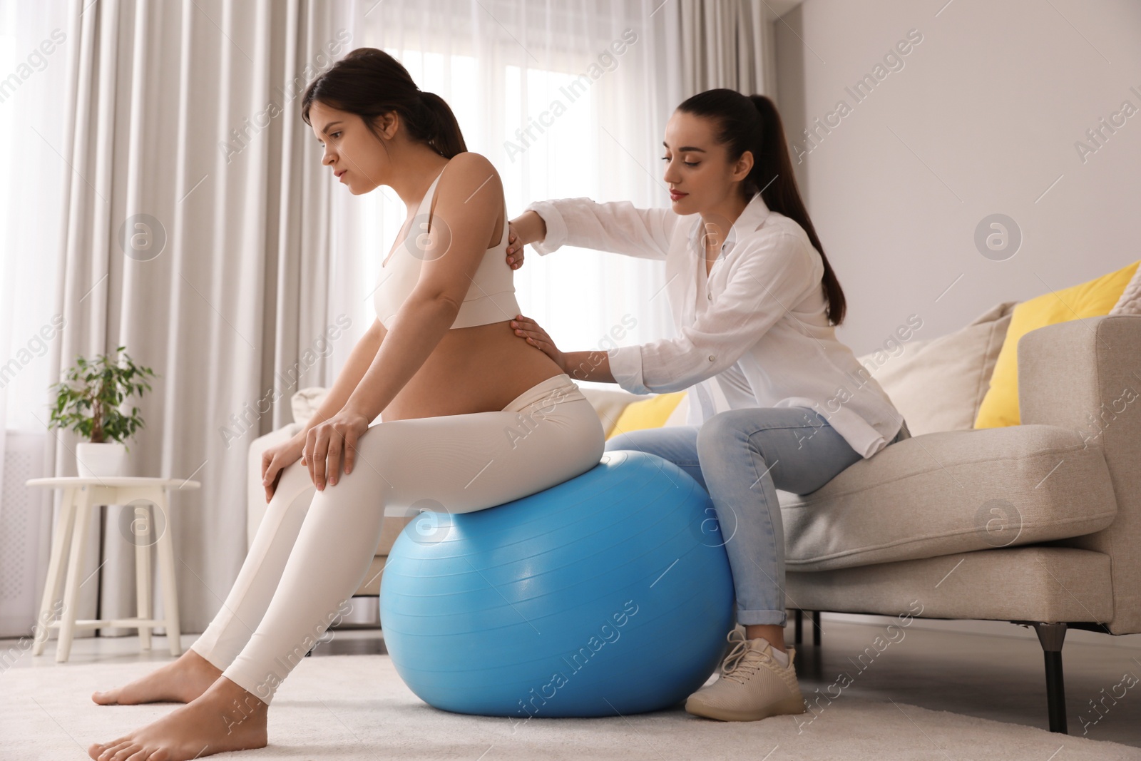 Photo of Doula working with pregnant woman in living room. Preparation for child birth