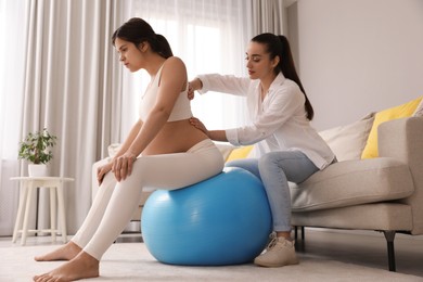 Doula working with pregnant woman in living room. Preparation for child birth