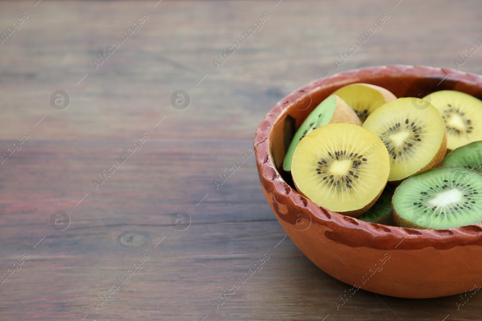 Photo of Bowl of many cut fresh kiwis on wooden table, closeup. Space for text