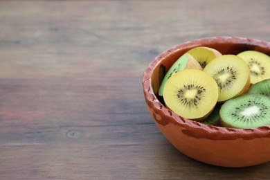 Photo of Bowl of many cut fresh kiwis on wooden table, closeup. Space for text