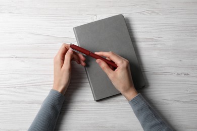 Woman with stylish notebook and pen at white wooden table, top view