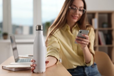 Woman holding thermos bottle at workplace, focus on container. Space for text