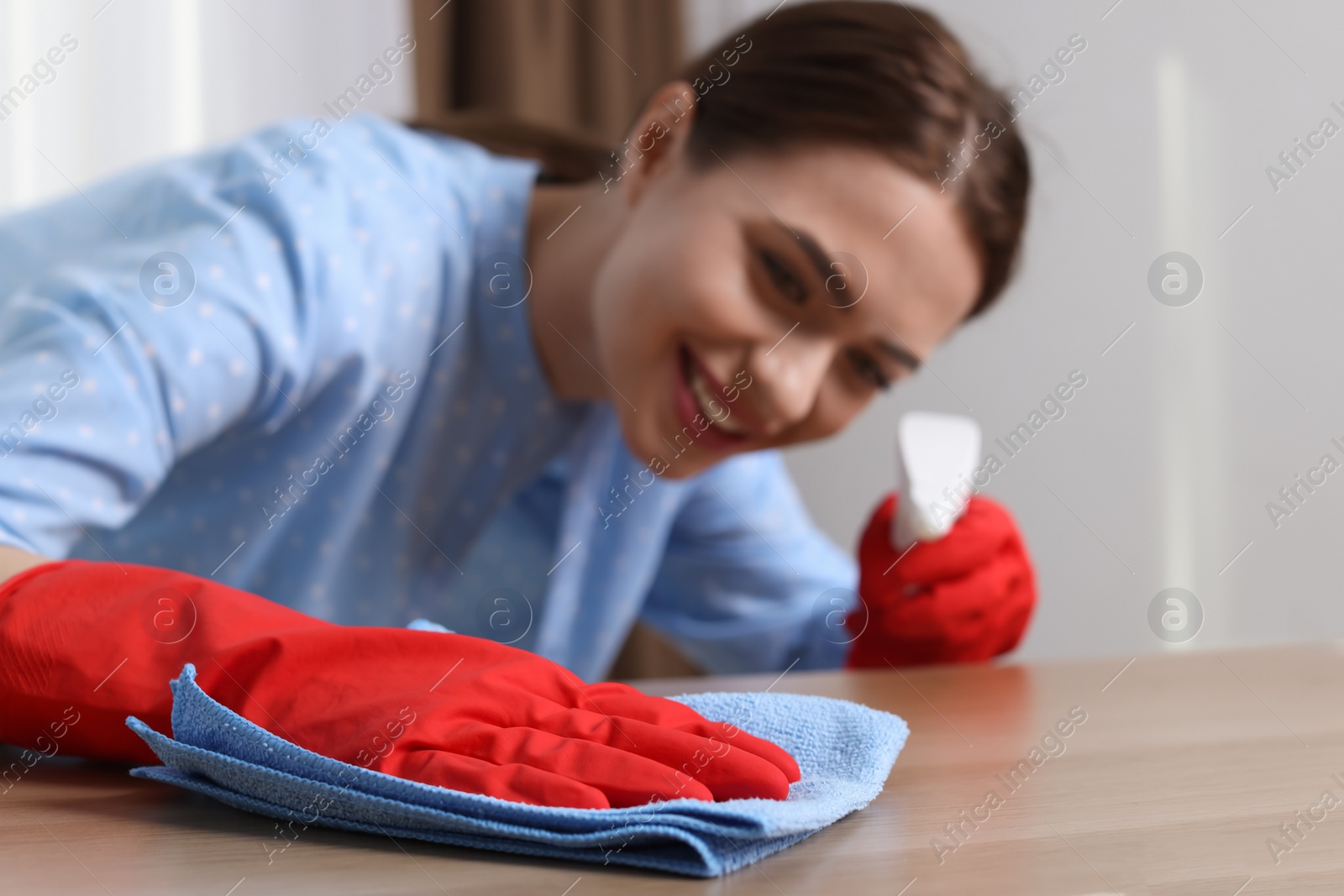 Photo of Young woman cleaning wooden table with rag at home, focus on hand