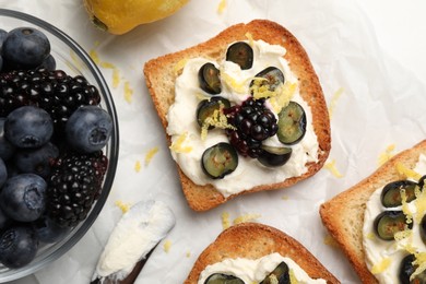 Photo of Tasty sandwiches with cream cheese, blueberries, blackberries and lemon zest on white table, flat lay
