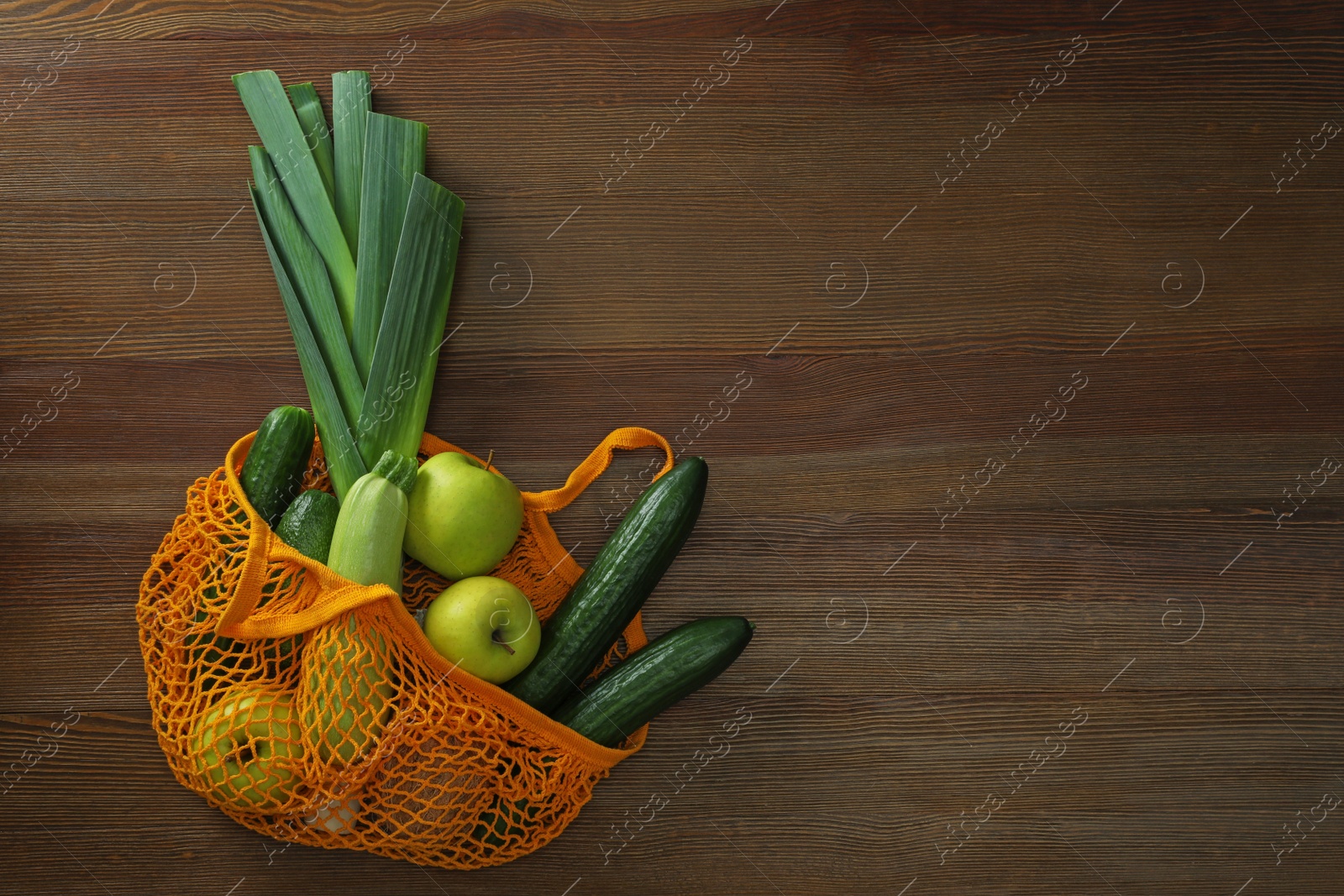 Photo of Net bag with vegetables and fruits on wooden table, top view. Space for text