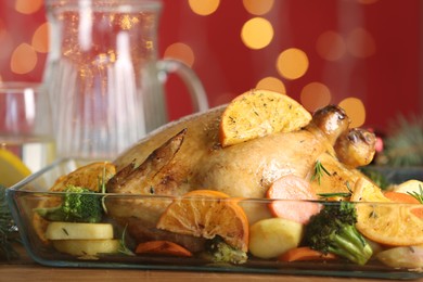 Photo of Delicious chicken with oranges and vegetables on table against blurred festive lights, closeup