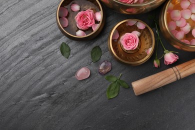 Photo of Tibetan singing bowls with water, beautiful rose flowers and mallet on gray table, flat lay. Space for text