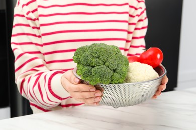 Photo of Woman holding colander with fresh vegetables at white marble table, closeup