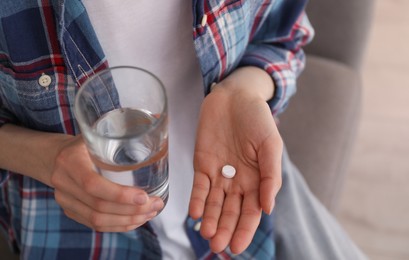 Photo of Young woman with abortion pill and glass of water indoors, closeup
