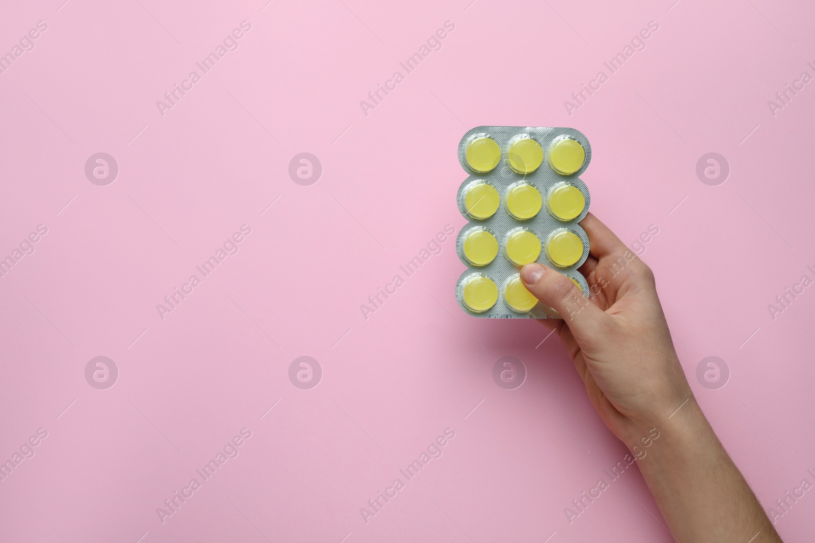 Photo of Woman holding blister with cough drops on pink background, top view. Space for text