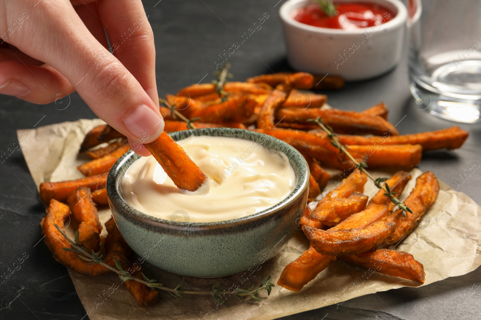 Photo of Woman dipping sweet potato fries into sauce at dark grey table, closeup