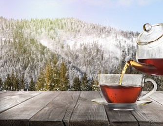 Image of Pouring tea into glass cup on wooden table and beautiful winter landscape on background