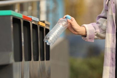 Photo of Woman throwing plastic bottle into sorting bin outdoors, closeup