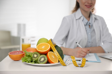 Photo of Nutritionist at desk with fruits, vegetables and measuring tape in office, closeup
