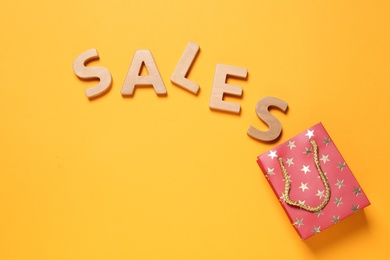 Photo of Word Sales of wooden letters near small paper bag on yellow background, flat lay