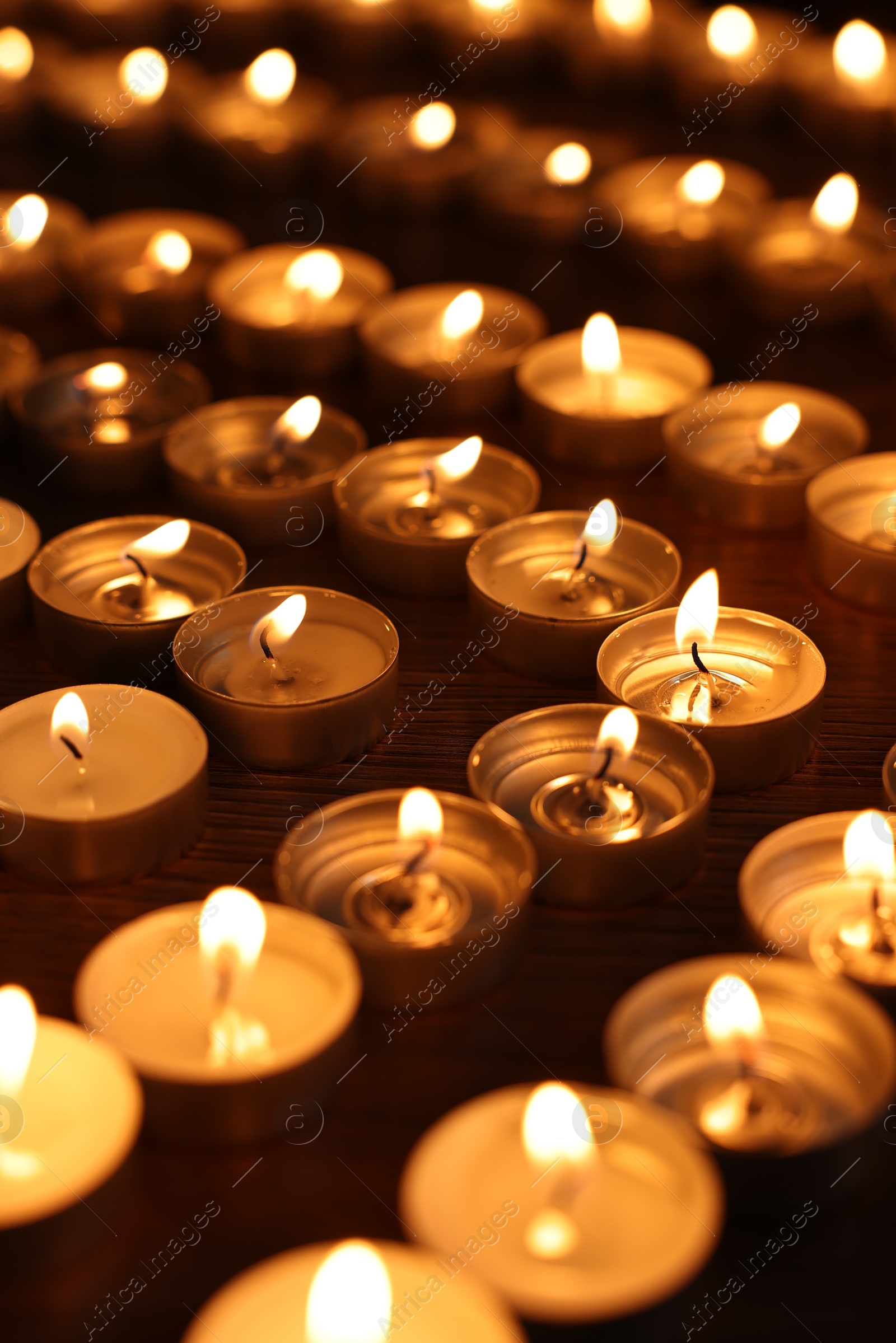 Photo of Burning candles on wooden table in darkness, closeup