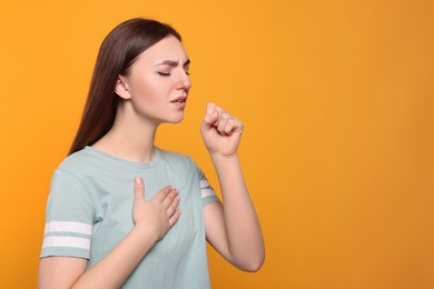 Photo of Young woman coughing on orange background, space for text. Sore throat