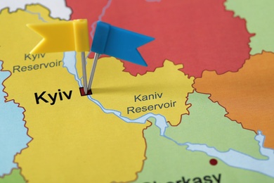 Map of Ukraine with blue and yellow flag push pins placed on Kyiv, closeup