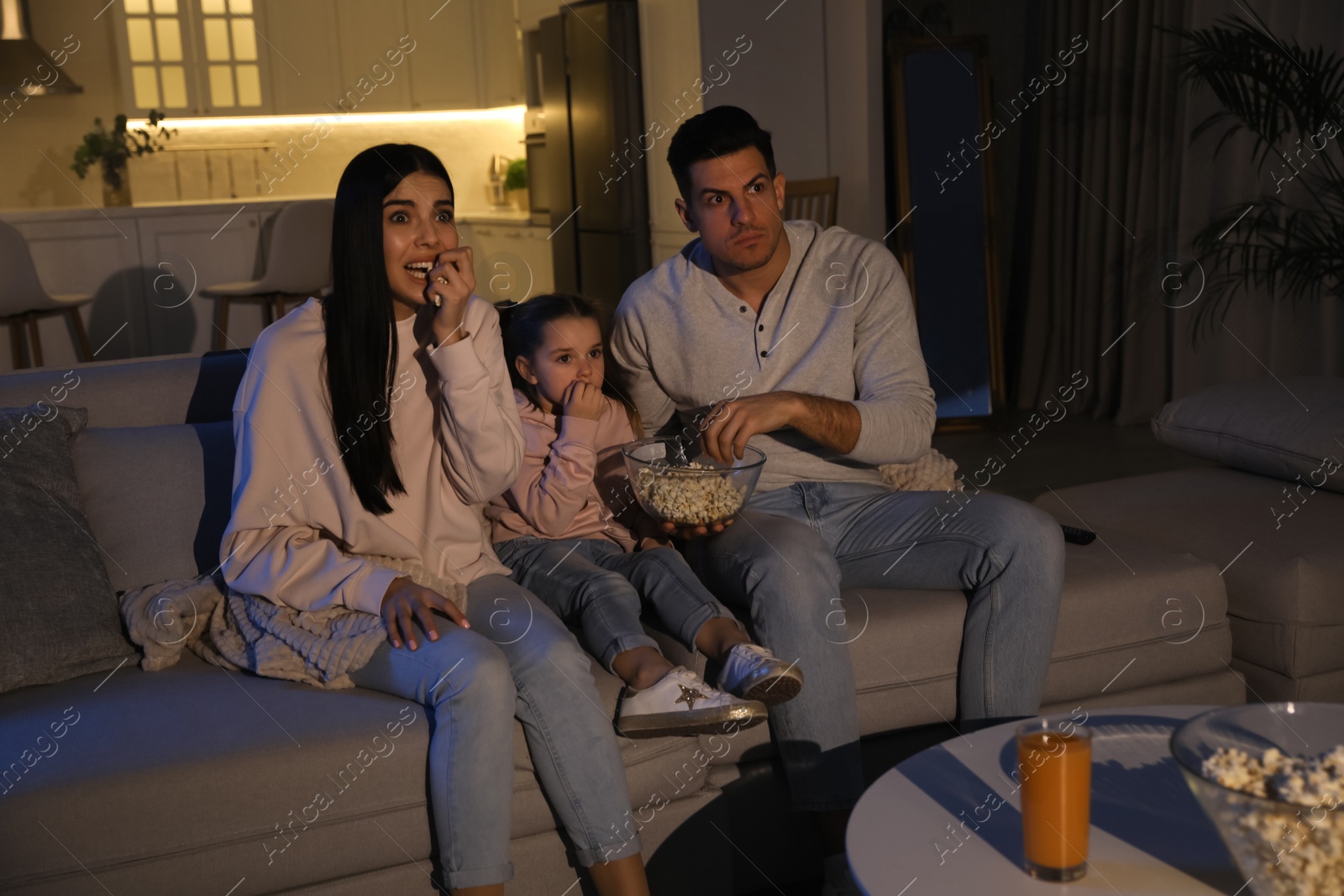 Photo of Family watching movie with popcorn on sofa at night