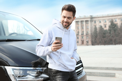 Photo of Handsome young man with smartphone near modern car outdoors