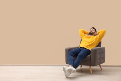 Photo of Handsome man relaxing in armchair near beige wall indoors, space for text