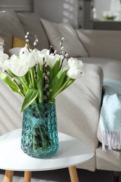 Beautiful bouquet of willow branches and tulips in vase on table indoors