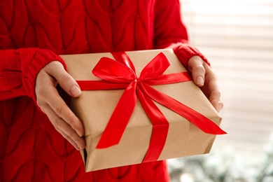 Photo of Woman holding Christmas gift box indoors, closeup