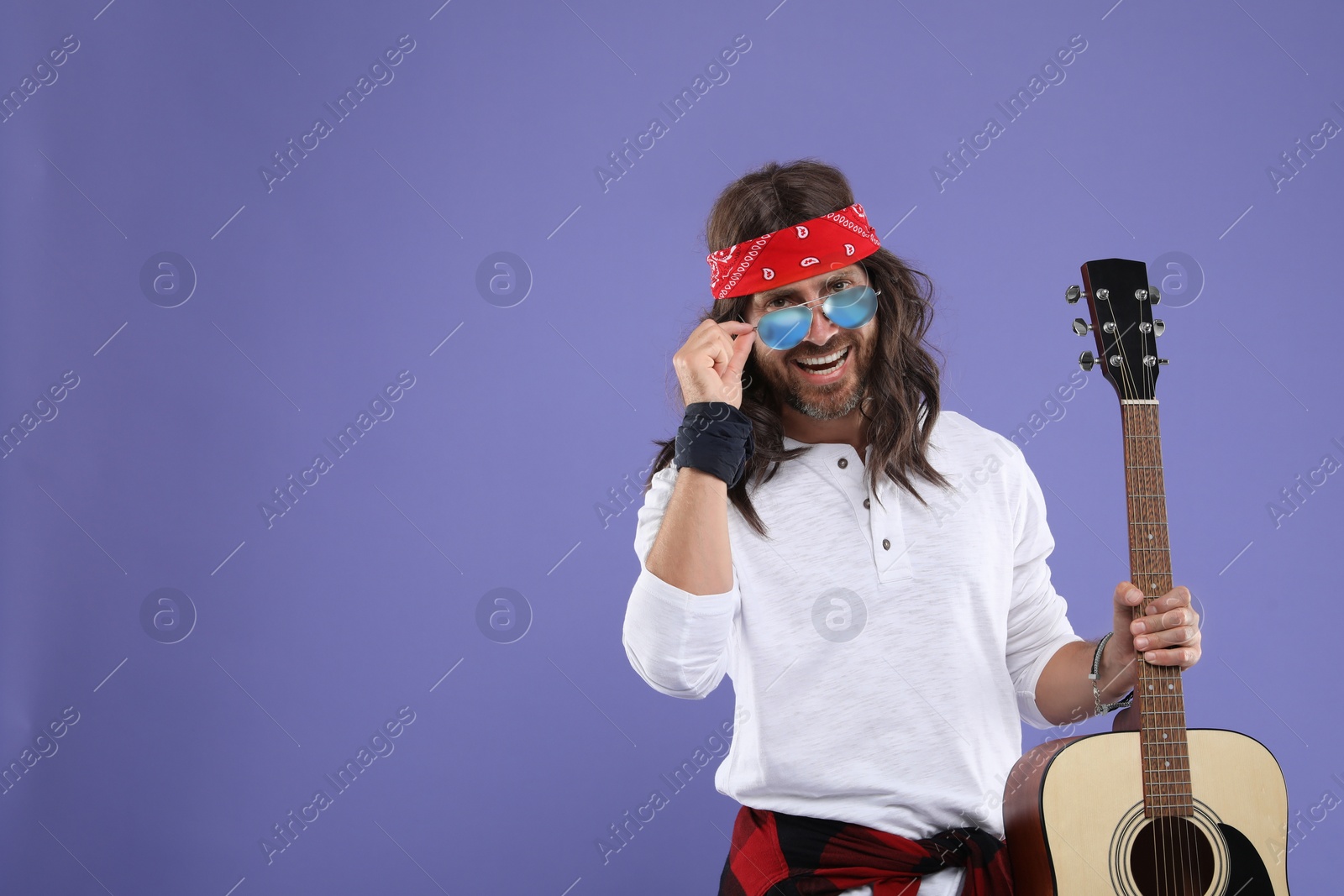 Photo of Stylish hippie man with guitar on violet background, space for text