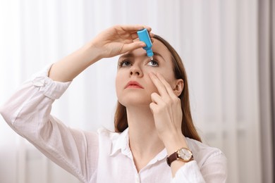 Photo of Young woman applying medical eye drops indoors
