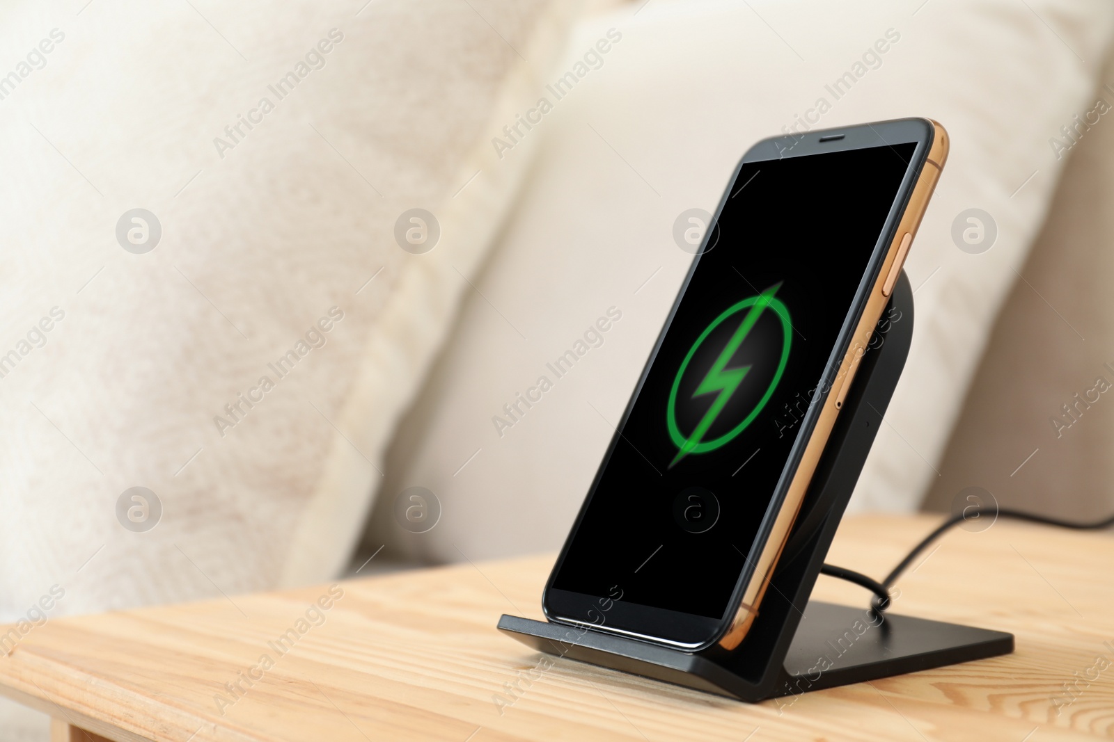 Photo of Modern mobile phone charging on wireless pad in bedroom, closeup. Space for text