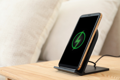 Photo of Modern mobile phone charging on wireless pad in bedroom, closeup. Space for text