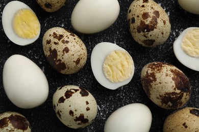 Photo of Peeled and unpeeled hard boiled quail eggs on black table, flat lay