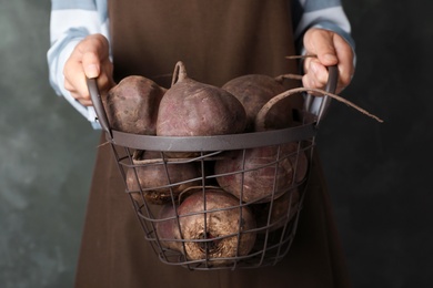 Photo of Woman holding metal basket with beets on grey background