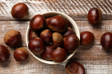 Photo of Sweet fresh edible chestnuts in bowl on wooden table, top view