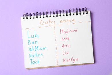 Photo of Notebook with lists of baby names on purple background, top view