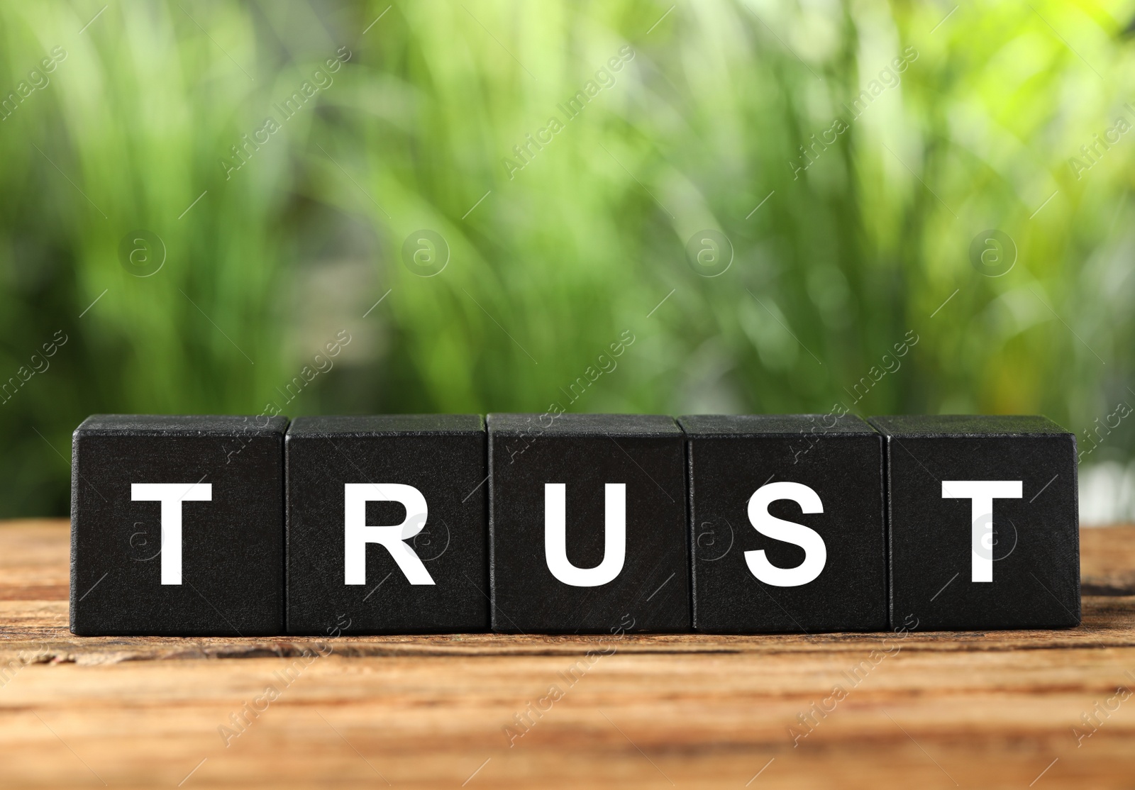 Photo of Word Trust made of black cubes on wooden table against blurred background