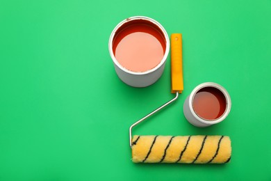 Photo of Cans of orange paint and roller brush on green background, flat lay. Space for text