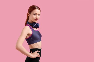 Woman in sportswear and headphones on pink background, space for text