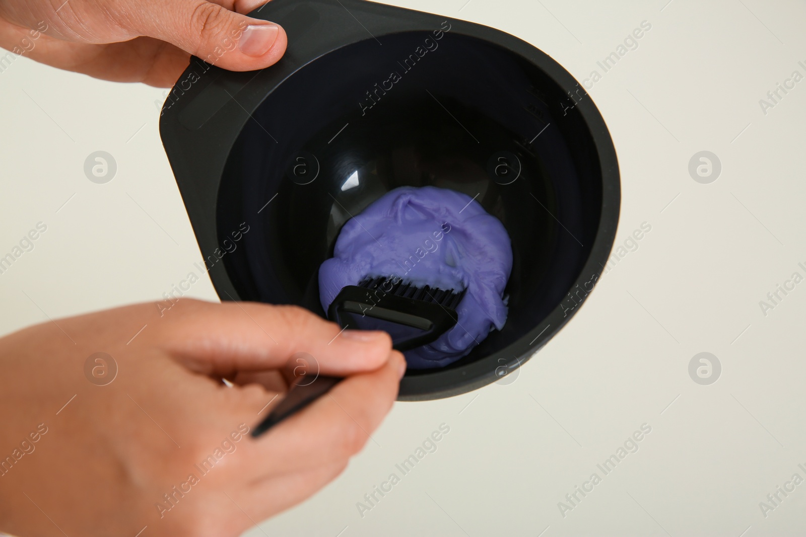 Photo of Woman preparing hair dye in bowl at white table, closeup