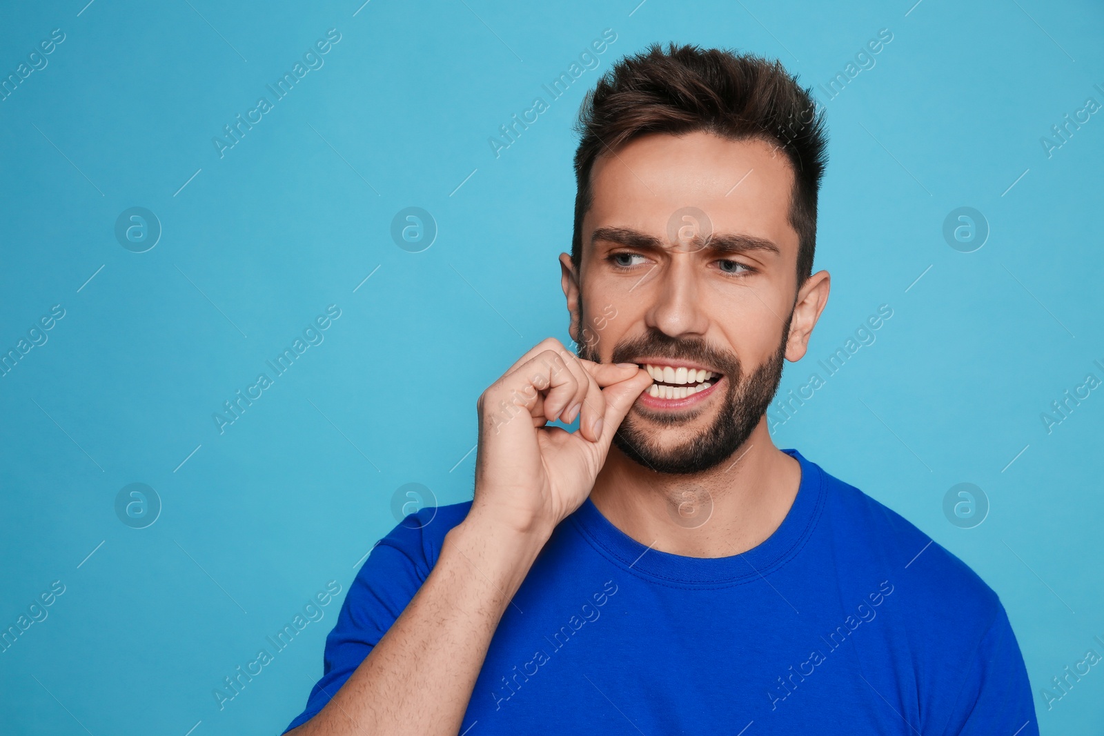Photo of Man biting his nails on light blue background. Space for text