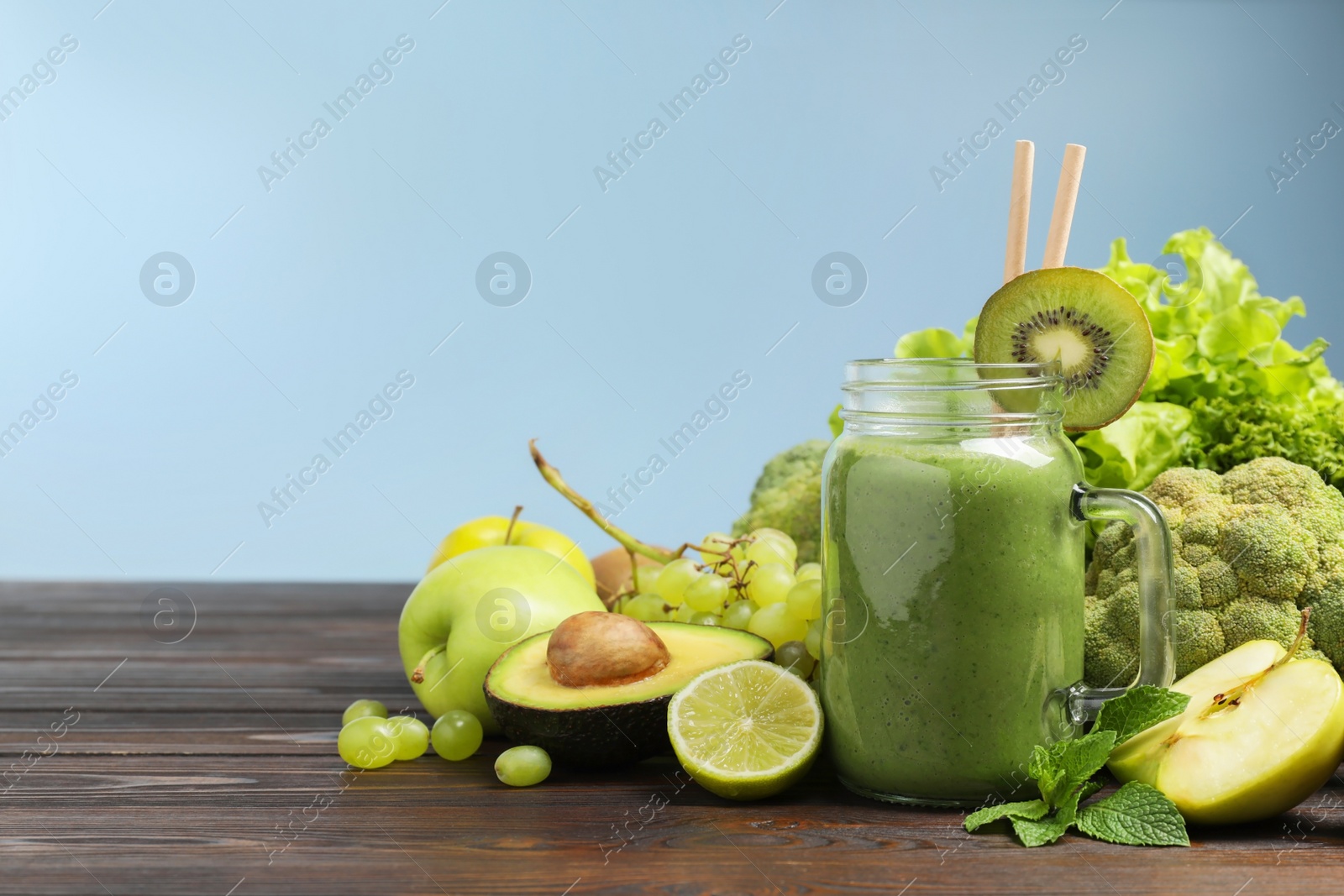 Photo of Green smoothie in mason jar and fresh ingredients on wooden table. Space for text