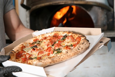 Photo of Chef holding delivery box with traditional oven baked Italian pizza in kitchen restaurant, closeup