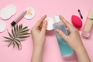 Woman with makeup remover, cotton pads, foundation, concealer and sponge on pink background, top view