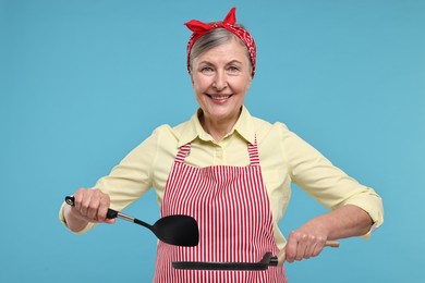 Photo of Happy housewife with turner and frying pan on light blue background