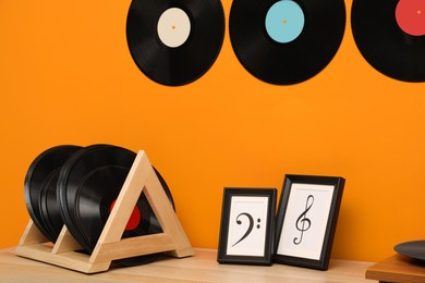 Vinyl records and pictures on wooden table near orange wall