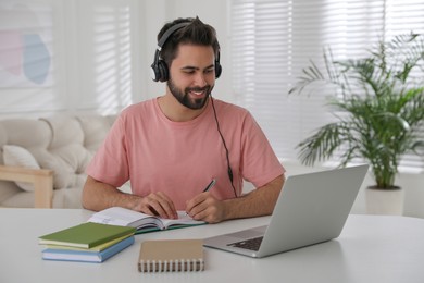 Photo of Young man watching webinar at table in room