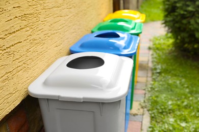 Many colorful recycling bins near yellow wall outdoors