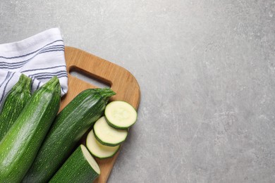 Whole and cut ripe zucchinis on light grey table, top view. Space for text